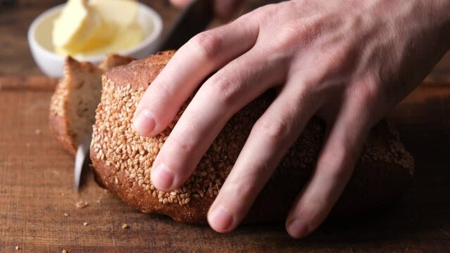 Closeup view cutting artisan bread on wooden board. Male hands cutting whole wheat sesame bread with a bread knife