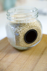 A glass jar of sesame seeds stands on a wooden cutting board