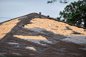 Wind damaged house roof with missing asphalt shingles after hurricane Ian in Florida. Repair of...