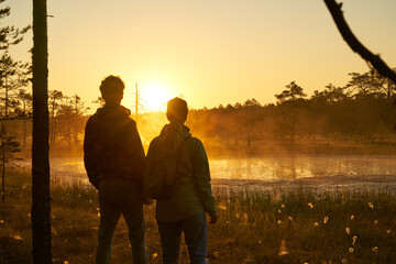woman and man holds hands tourist meets dawn in nature. Sunset,  light and fog, Reflections of trees in lakes . Travel romance. Viru swamps Estonia.