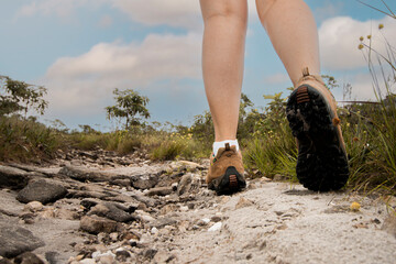Perna de Mulher branca andando  de bota sobre as pedras na trilha