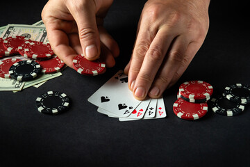 The player points with his finger at a winning four of a kind or quads combination in poker game on a black table with chips and money in club