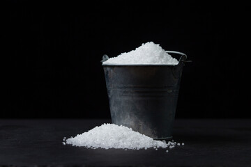 Large rock sea salt on a black background. Small steel bucket full of salt