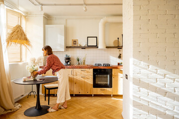Woman puts flowers on a dinner table, decoration and having some house chores at home. Sunny...