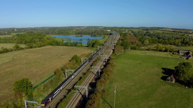 ENGLAND. passenger train passing through countryside. Modern high speed train. High speed passenger railway train South of England, UK. Fast train aerial shot. AERIAL: High speed train train. 