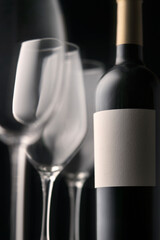 Fragment wine glasses and a bottle of red wine with a white label without an inscription. Beautiful still life, dark background, atmospheric mood, vertical photography.