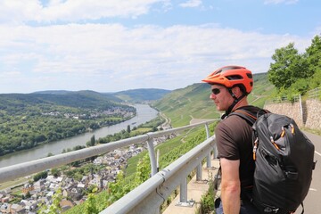 Man with bright orange bike helmet looking out over a panoramic view of the Moselle river