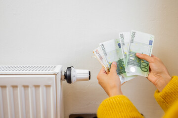 Person holding euro banknotes near heater at home. Concept of expensive energy resources and the...