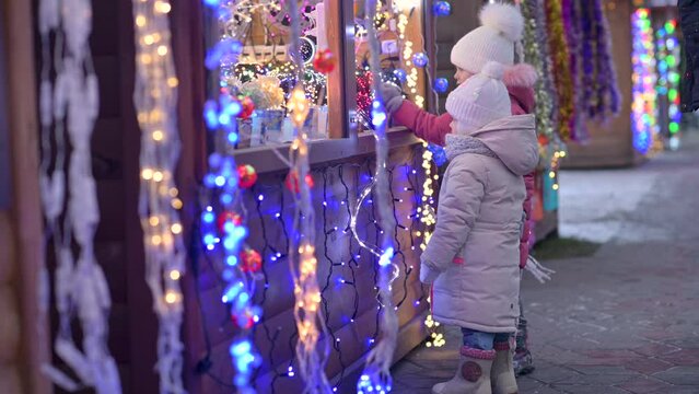 Two little cute girls are walking and admiring the Christmas decorations at the street Christmas fair