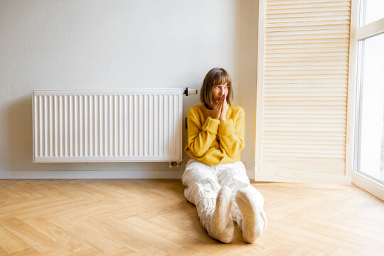 Woman Feeling Cold, Sitting On Floor Near Radiator At Home. Concept Of Saving Energy Resources And The Energy Crisis