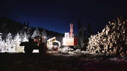 Night time industrial wood logging operation machinery moving around.