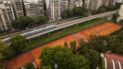 Train passing on railroad between Libertador Avenue and tennis court at Barrancas de Belgrano, Buenos Aires. Aerial drone view