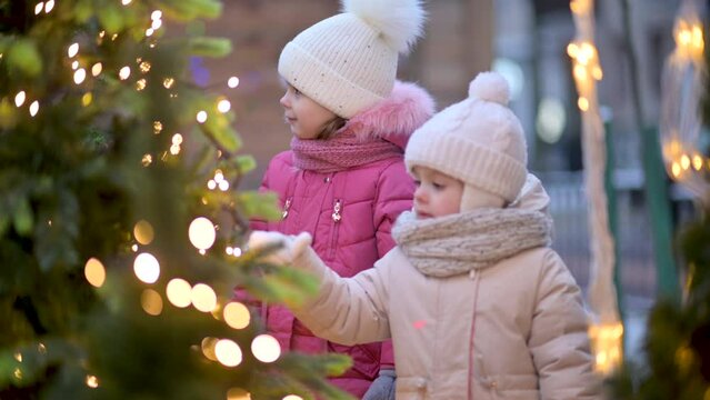 Two little cute girls are walking and admiring the Christmas decorations at the street Christmas fair