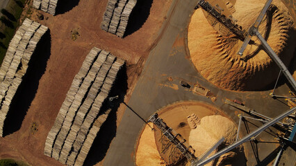 Aerial view showing heap of sawdust and stacked piles of trunks in paper mill factory - obrazy, fototapety, plakaty
