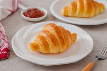 Fresh croissant on white plate and jam on table.