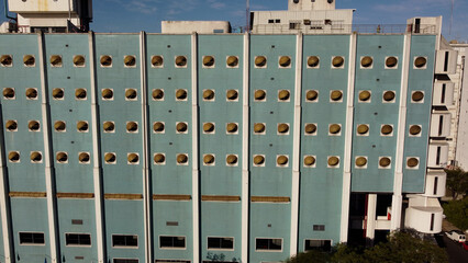 Aerial flight showing blue colored facade of building lighting in sun with circular windows -...
