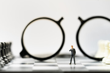 Miniature people, businessman thinking on chessboard with broken glasses. Business and financial concept