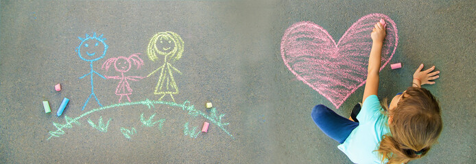 the child paints chalk on the asphalt heart. Selective focus.
