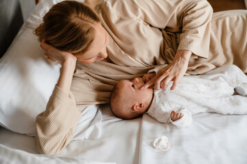 White young woman in housecoat lying in bed with her newborn baby