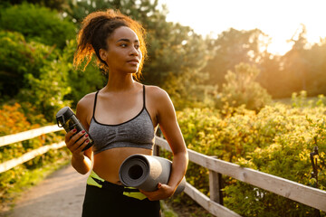 Young black woman walking with yoga mat after practice in summer park