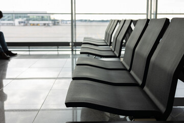 Naklejka na ściany i meble Silhouette shot and selective focus with copy space of waiting chairs or benches in the airport with background of clear window of runway for travelling flight due to vacation and business trip.