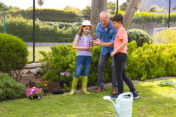 Caucasian children and grandfather spending time together in the garden, planting - Powered by Adobe