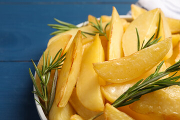 Plate with tasty baked potato wedges and rosemary on blue table, closeup