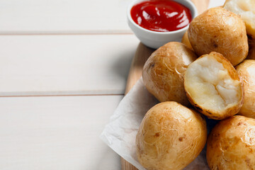 Tasty whole baked potatoes and sauce on white wooden table, closeup. Space for text
