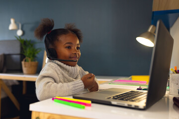 Happy african american girl learning, using laptop and headphone at home
