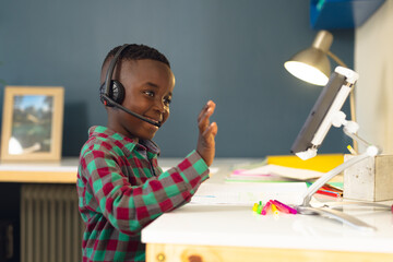 Smiling african american boy learning, using headphones and tablet at home