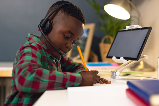 Smiling african american boy learning, using headphones and tablet with copy space at home