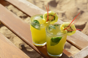 Glasses of refreshing drink with kiwi and mint on wooden bench at beach