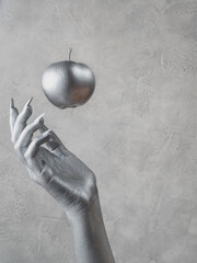Woman's hand with silver skin catches a silver apple. Close-up, copy space