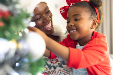African american mother and daughter spending time together and decorating christmas tree