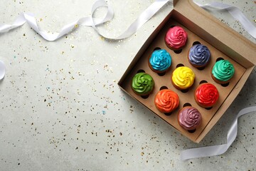 Box with delicious colorful cupcakes, ribbon and confetti on light grey table, flat lay. Space for text