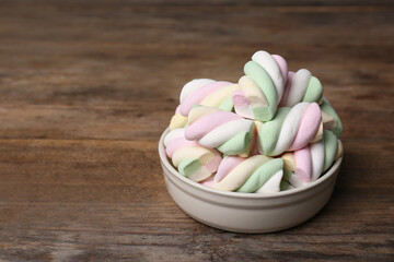 Bowl with colorful marshmallows on wooden table, space for text