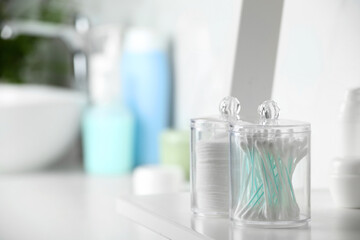 Containers with cotton swabs and pads on white shelf in bathroom. Space for text