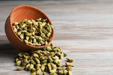 Overturned bowl with dry cardamom pods on wooden table, closeup. Space for text