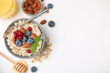 Oatmeal served with berries, almonds and honey on white background, flat lay. Space for text