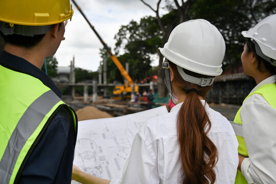 Rear view image of Civil engineers and foreman in helmet and vest checking a building project on the construction site.