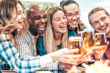 Obraz premium Happy friends toasting beer at brewery bar - Multiracial people clinking glasses with brew at house party - Concept about young people having fun together