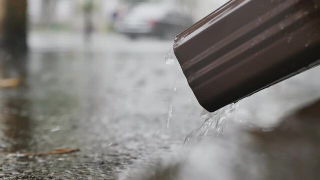 close-up the stream of water flows down the drainpipe from top to bottom. Fall of water on the asphalt flowing down from the roof of a residential building. The water drain system is working properly