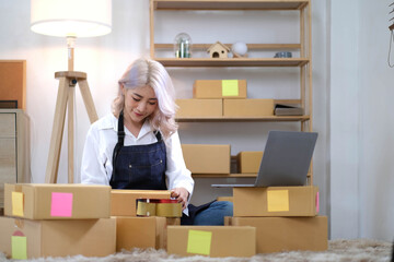 Young beautiful happy asian business woman owner of SME online using laptop receive order from customer with parcel box packaging at her startup home office, online business seller and delivery