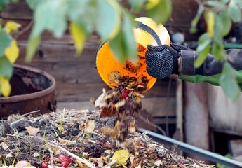 A woman throws kitchen waste into a compost heap with layers of organic matter, old grass and soil....