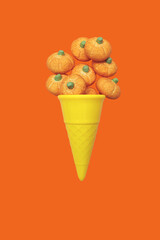 Halloween minimal concept with orange background small candy pumpkins as ice cream cone levitation on wallpaper with copy space. Holiday autumn idea for party invitation. Spooky holiday symbol.