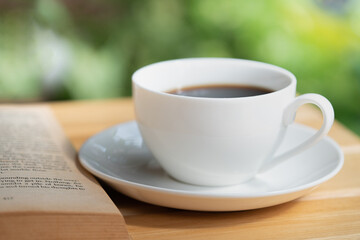 A cup of coffee and book on wooden table in garden with green nature background