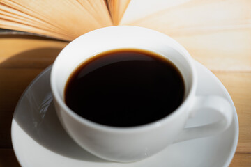 A white cup of black coffee and book on wooden table