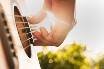 Close up hand playing acoustic guitar on sunset nature background