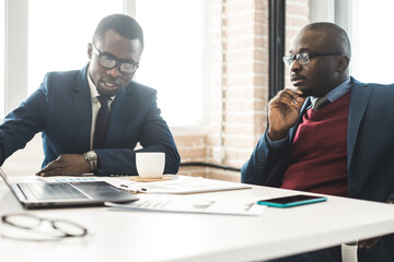 Two dark-skinned partners of an African American businessman in a meeting work on a laptop in the office. Affordable private courses and distance learning