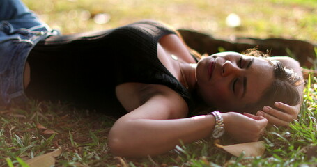 Woman lying on grass outside dreaming. Relaxed tranquil girl lied outdoors